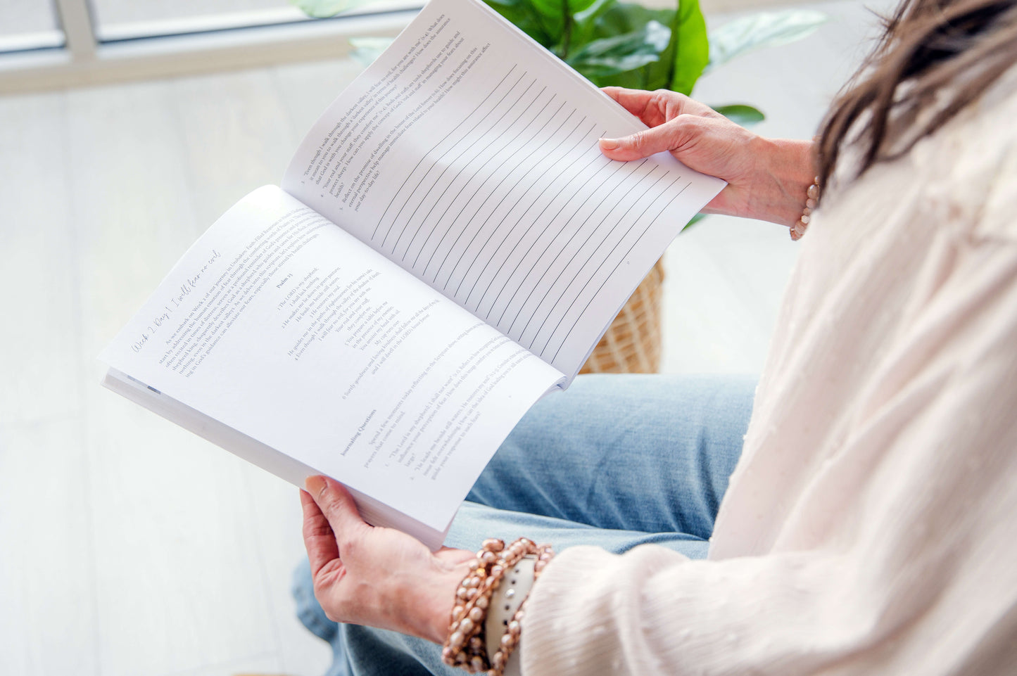 Person reading a book in a cozy indoor setting with a plant in the background