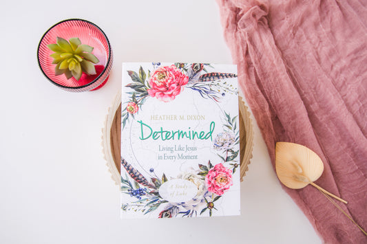 Book titled 'Determined' with floral design on a white surface with pink fabric and plant.