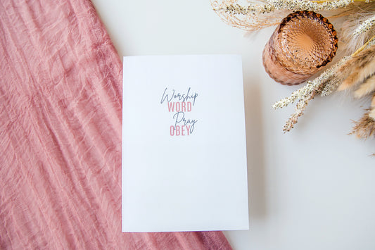 White card with 'Worship Word Pray Cry' text on a pink fabric background